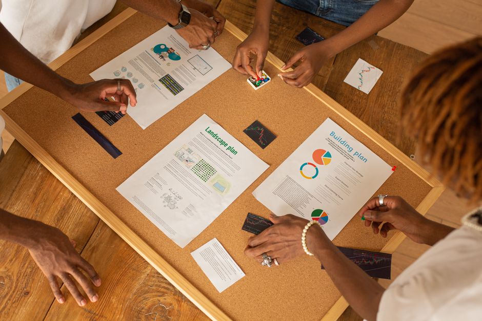 A diverse team collaborates on a workspace board with charts and plans.
